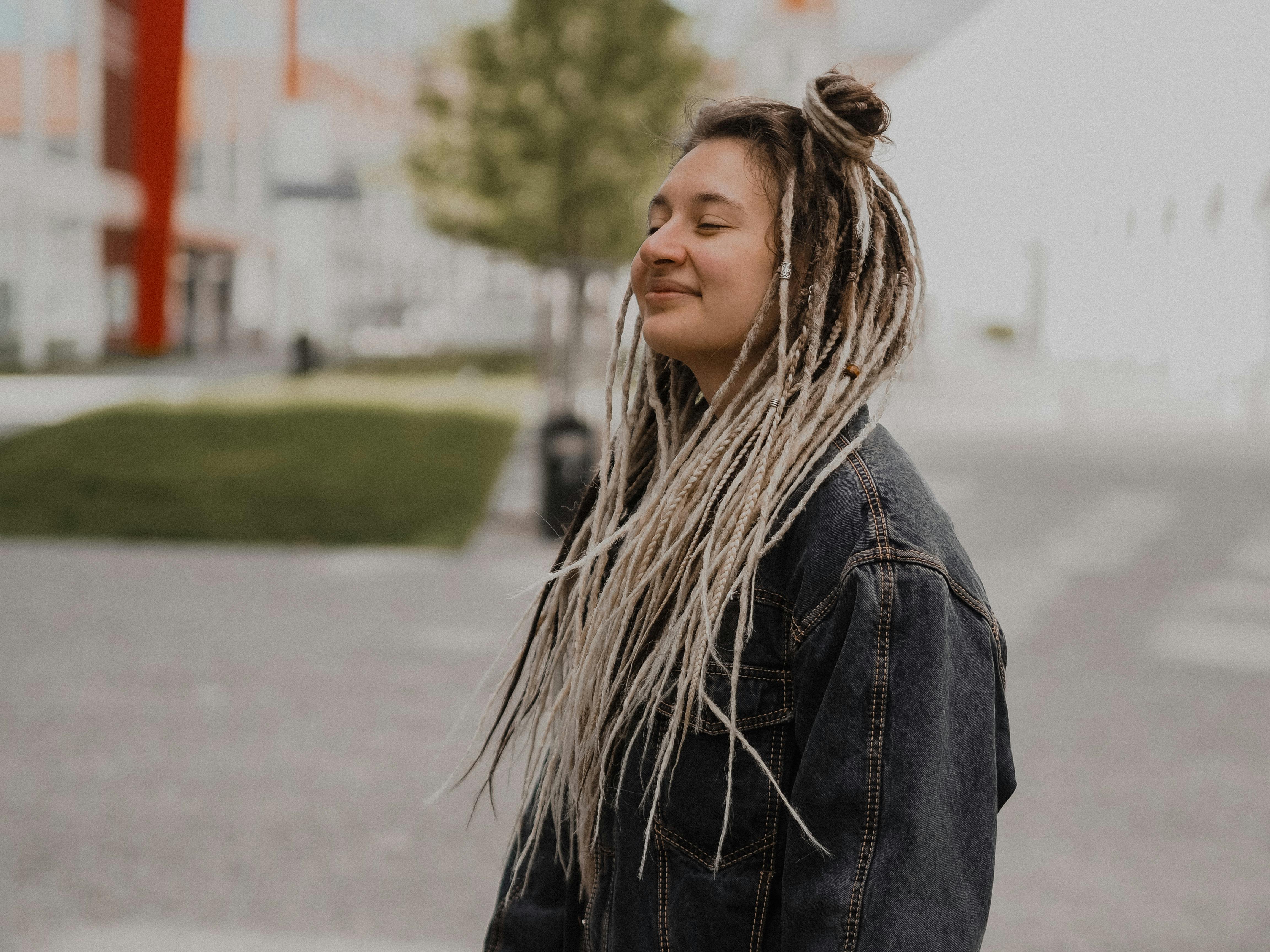 calm female with dreadlocks standing with closed eyes on city street