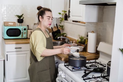 Free Asian woman preparing a meal in a cozy kitchen with modern appliances. Stock Photo