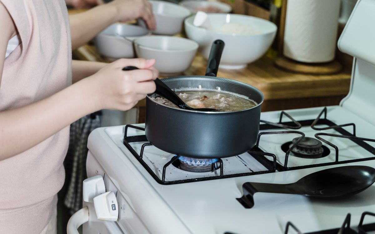 Close-up of a woman stirring soup on a gas stove in a home kitchen.