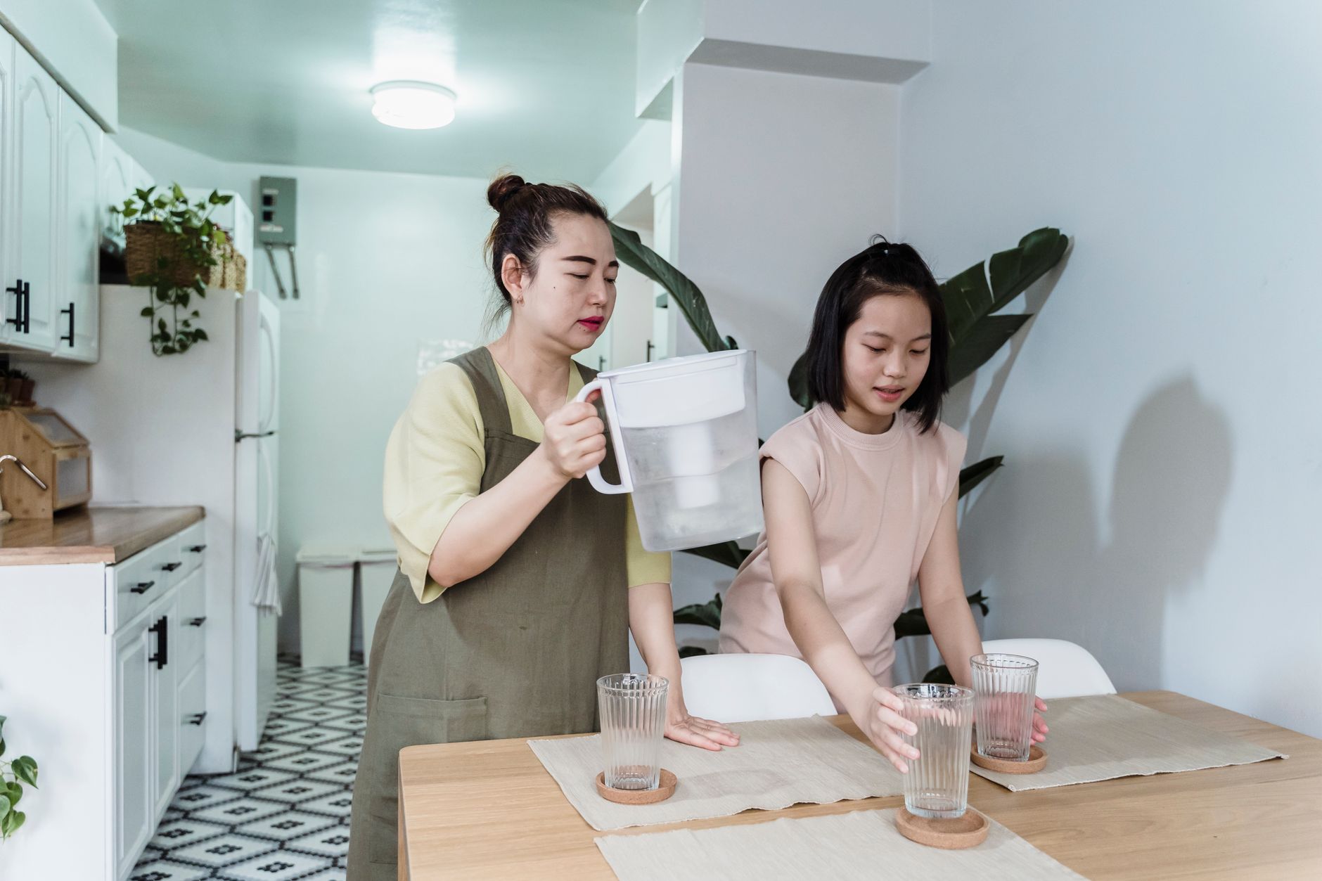 A woman and a girl set a dining table together indoors, fostering family bonding.
