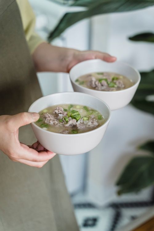 Free Close-up of hands holding two bowls of delicious homemade soup garnished with herbs. Stock Photo