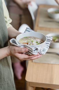 Close-up of a person holding a warm, homemade soup in a white bowl with a towel.