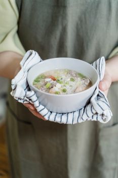 Close-up of a person holding a warm bowl of soup with green onions and vegetables.