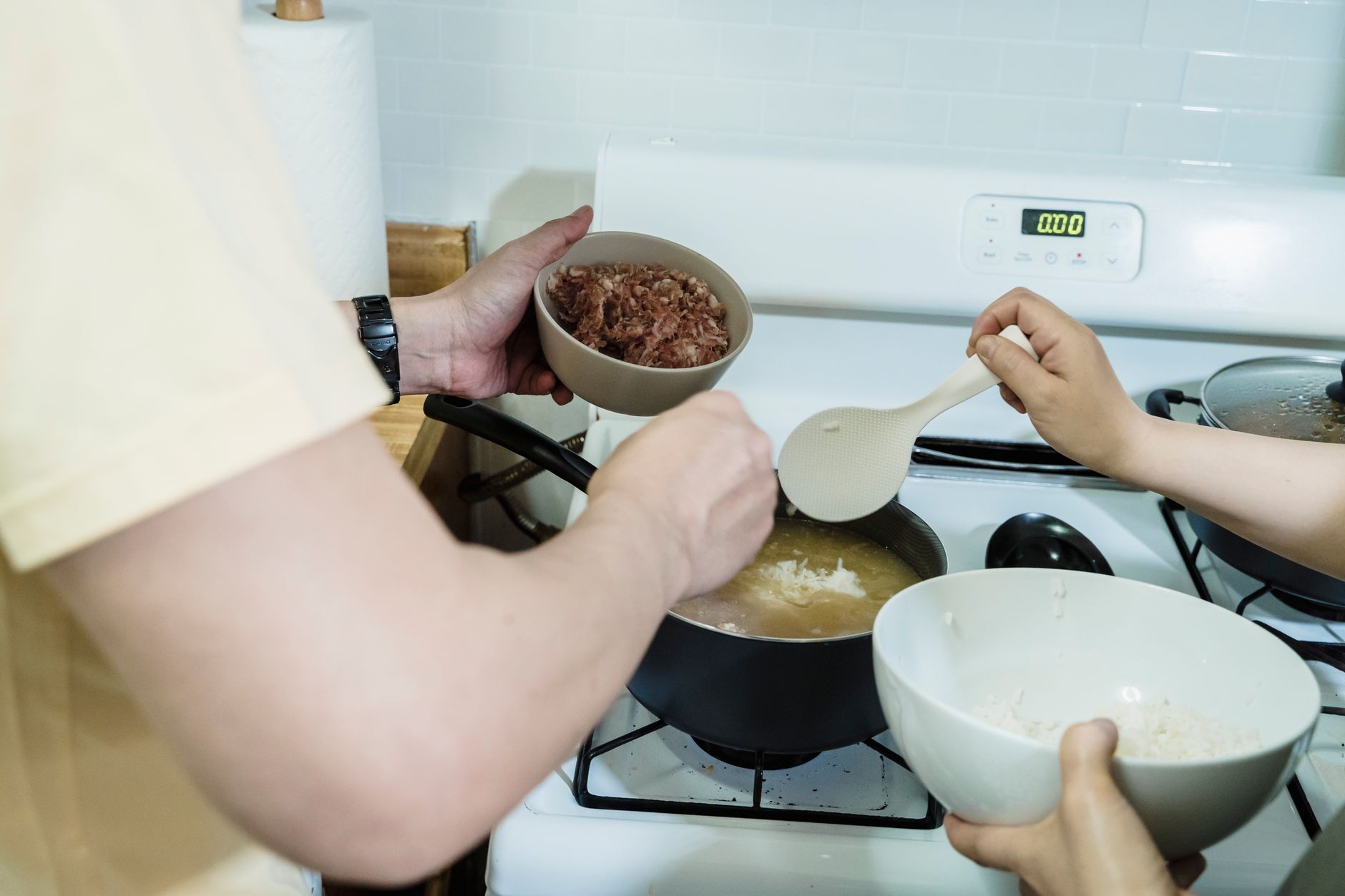 Close-up view of hands adding ingredients into pot on stove, preparing a meal.