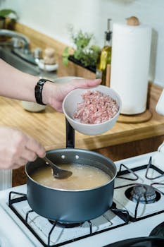 A person cooking homemade soup with ground pork in a kitchen.
