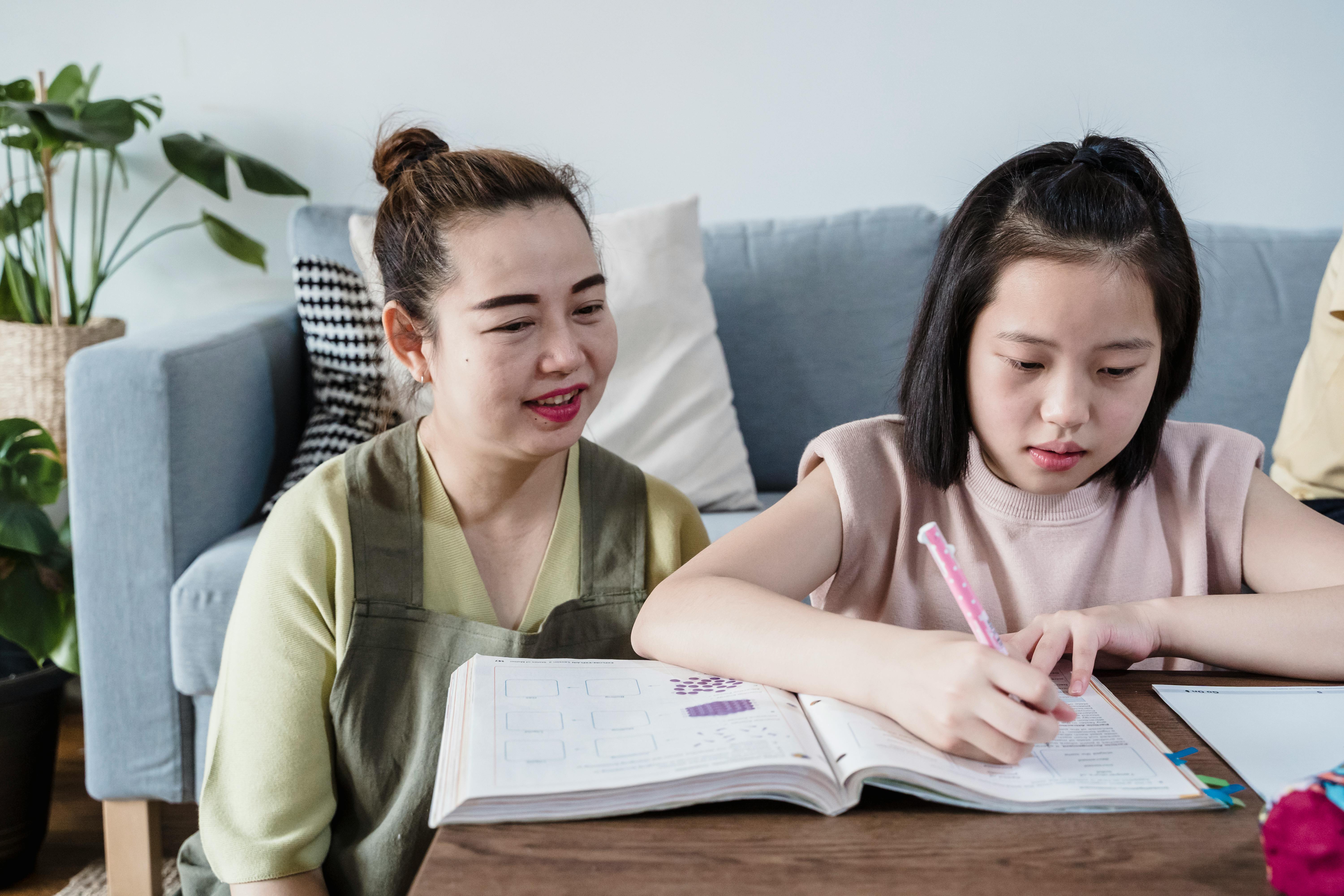 a mother looking at her daughter writing on the book