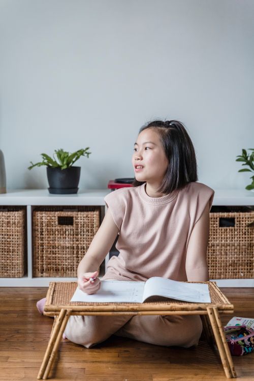 Free A young girl sitting on the floor studying indoors with an open notebook. Stock Photo