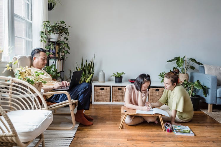 A Woman Helping Her Daughter With Her Homework While Sitting On The Floor