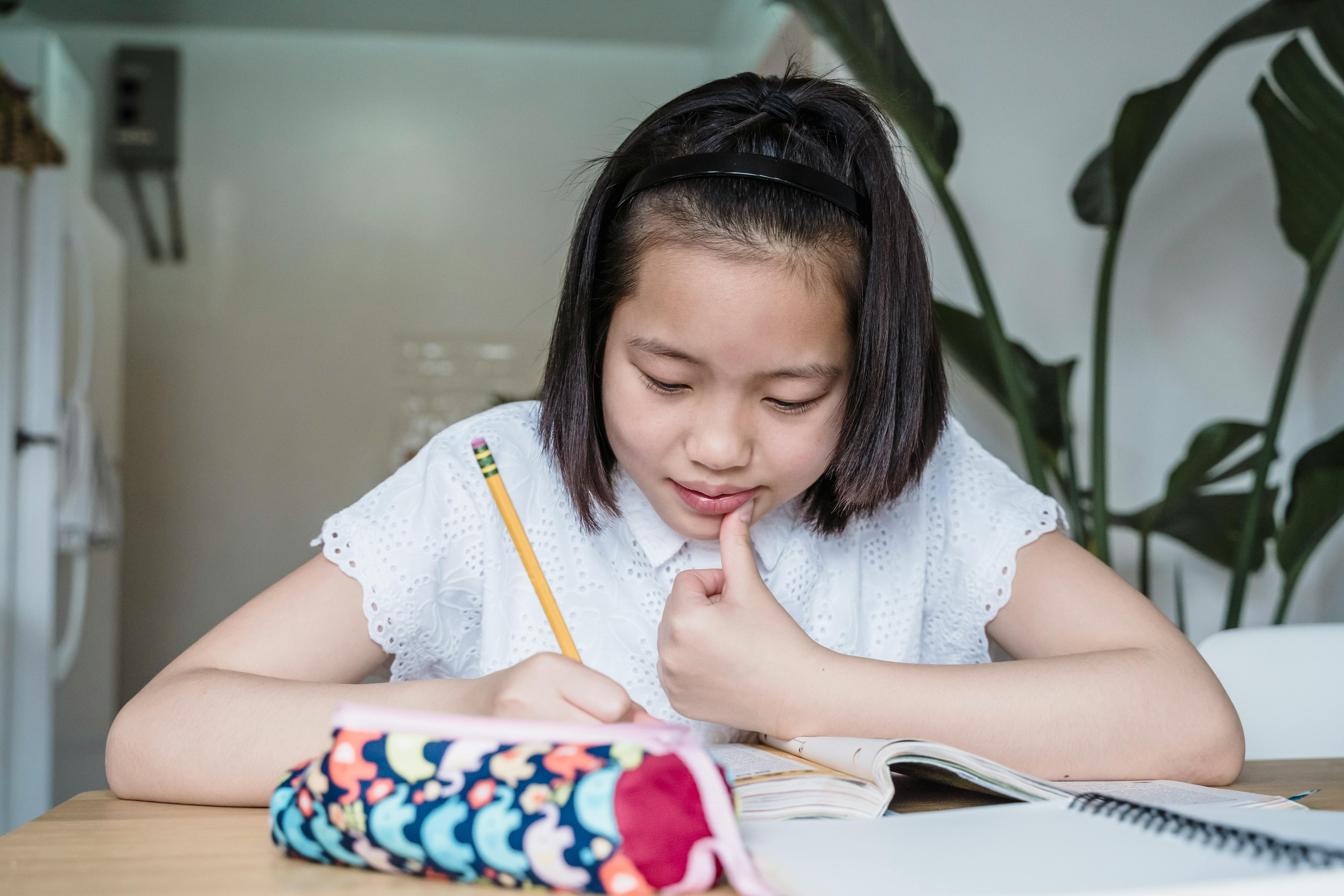 A young girl focuses on her homework while seated at a desk inside a cozy home setting.