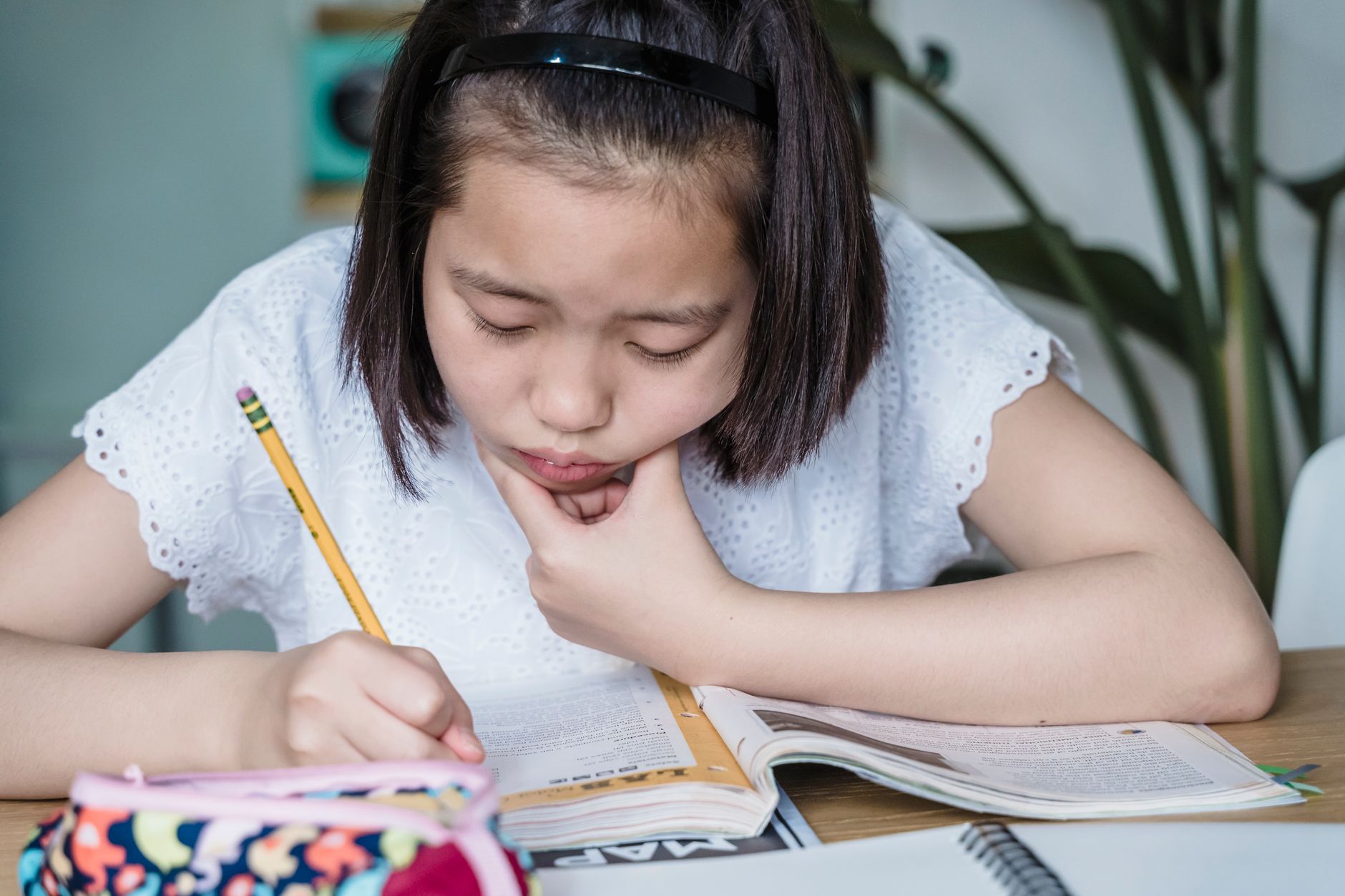 A young girl deeply engaged in homework, writing in a notebook at home.