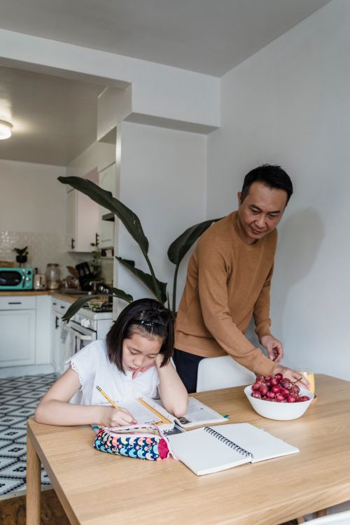Free Father helps daughter with homework in a cozy kitchen setting. Stock Photo