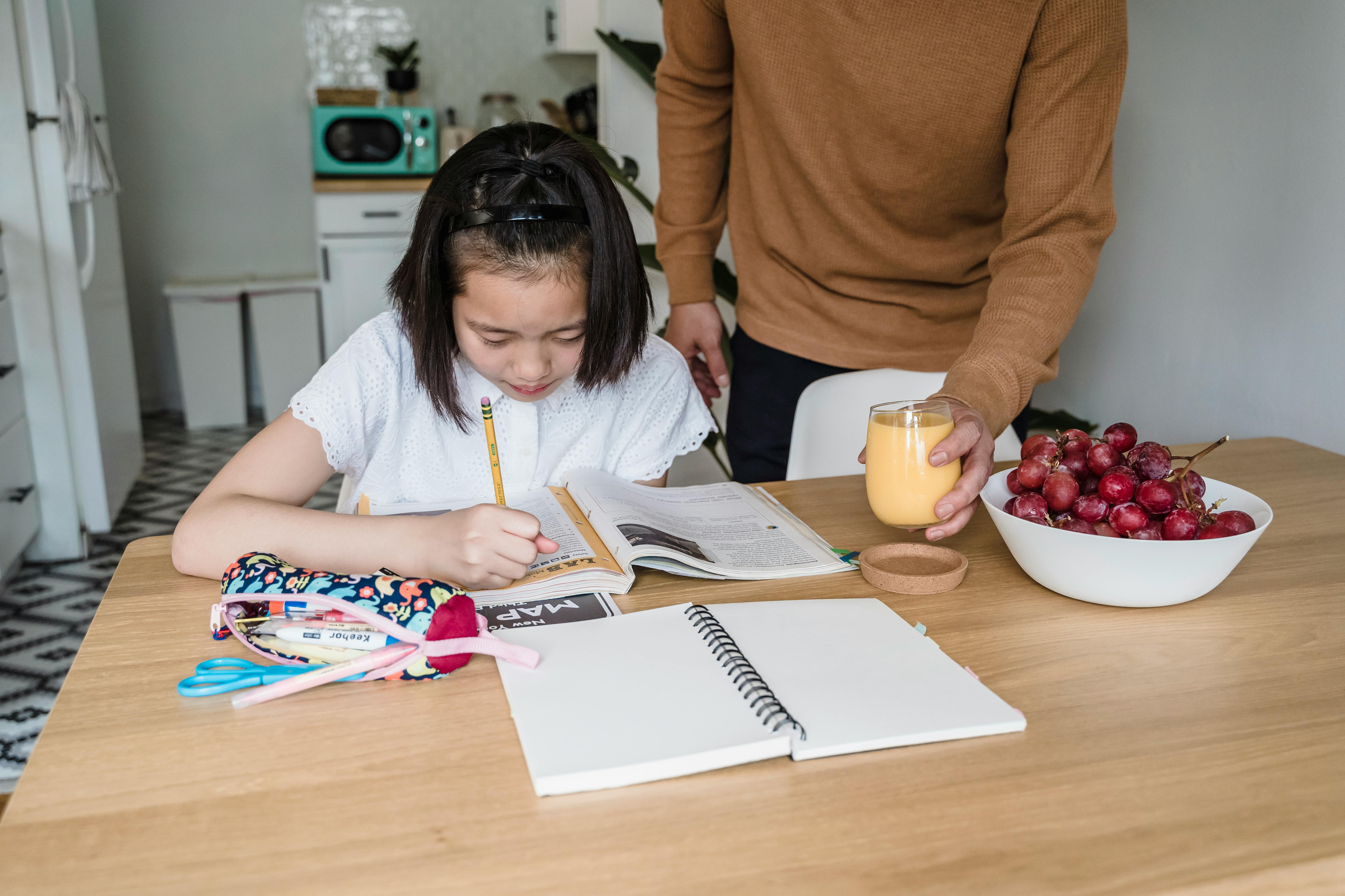 A man and a young girl sit at a table, engaged in reading a book together, promoting learning and connection.