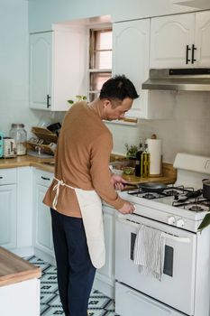 A man in a brown sweater and apron cooking on a modern kitchen stove.