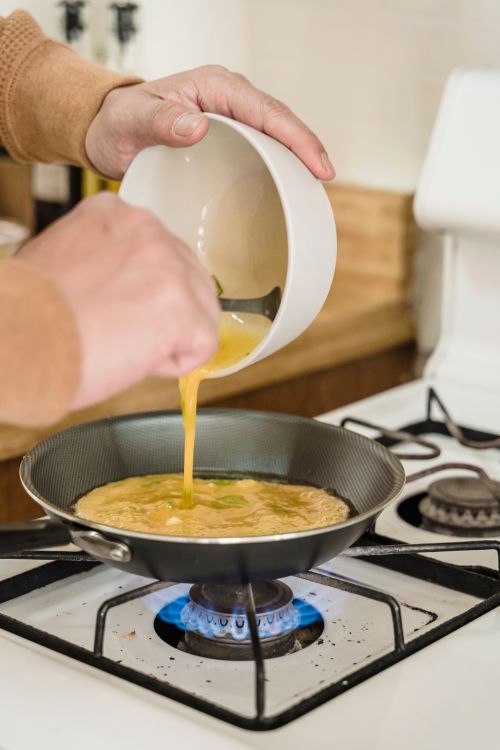 Free Person making an omelet in a frying pan over a gas stove indoors, showcasing cooking process. Stock Photo
