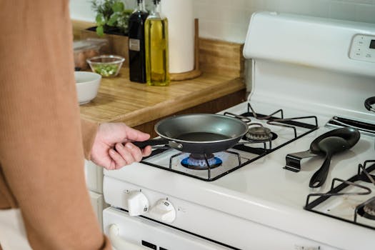 Close-up of a frying pan held over a gas burner on a stove, with kitchen essentials nearby.