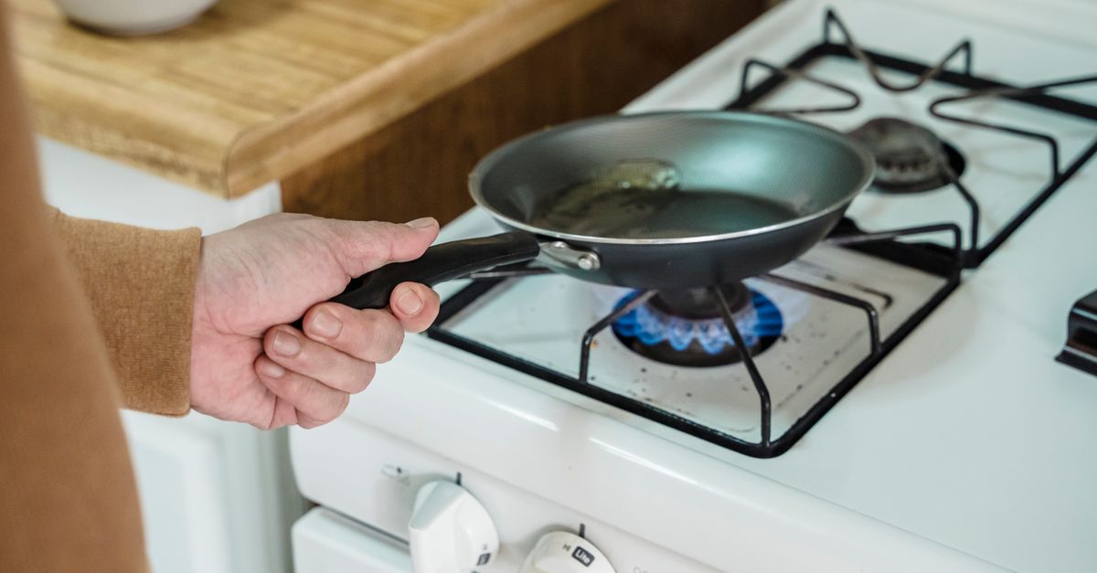 Close-up de uma mão segurando uma frigideira sobre um fogo a gás na cozinha