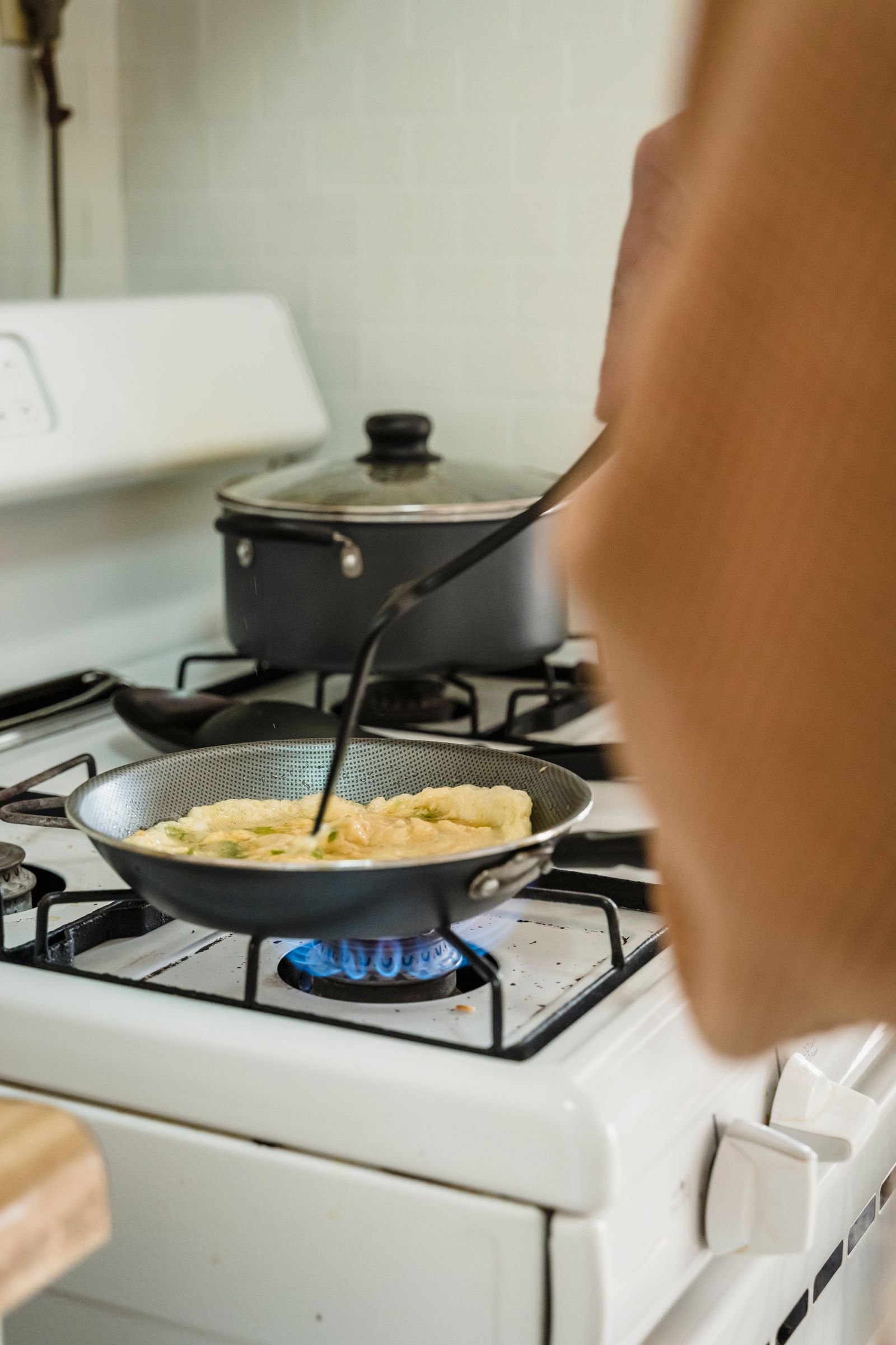 Preparing scrambled eggs on a gas stove with frying pan and spatula.