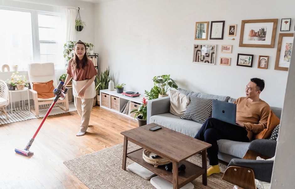 Top Robot Mop and Vacuum Combos for Hard Floors (2025 Review) A man and woman indoors, one cleaning, the other using a laptop, in a modern living room.