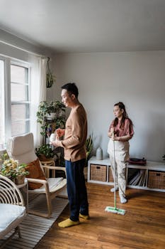 A couple cleaning their cozy, plant-filled living room together.