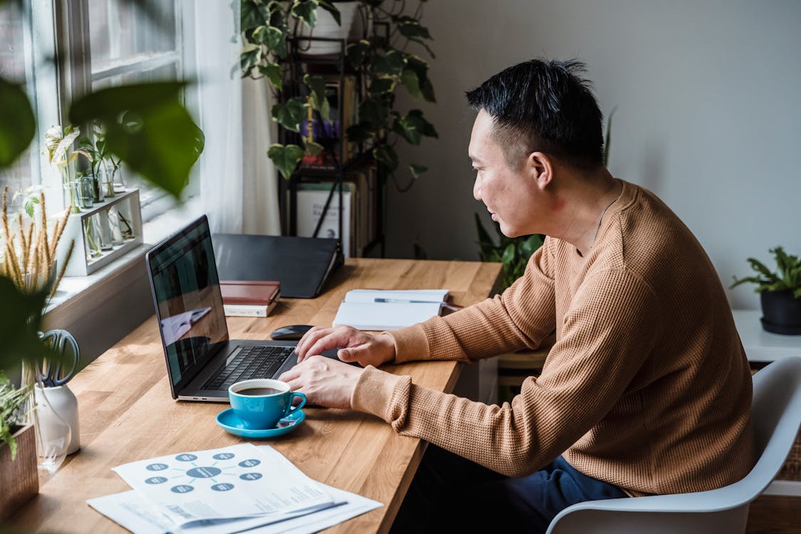 Free Man in Brown Sweater Sitting at Table Using Ipad Stock Photo