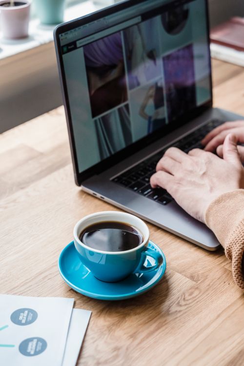 Free Hands typing on laptop beside a cup of coffee on a wooden desk. Stock Photo