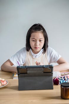 Asian teen girl using a digital tablet for online learning at home, focused and engaged.