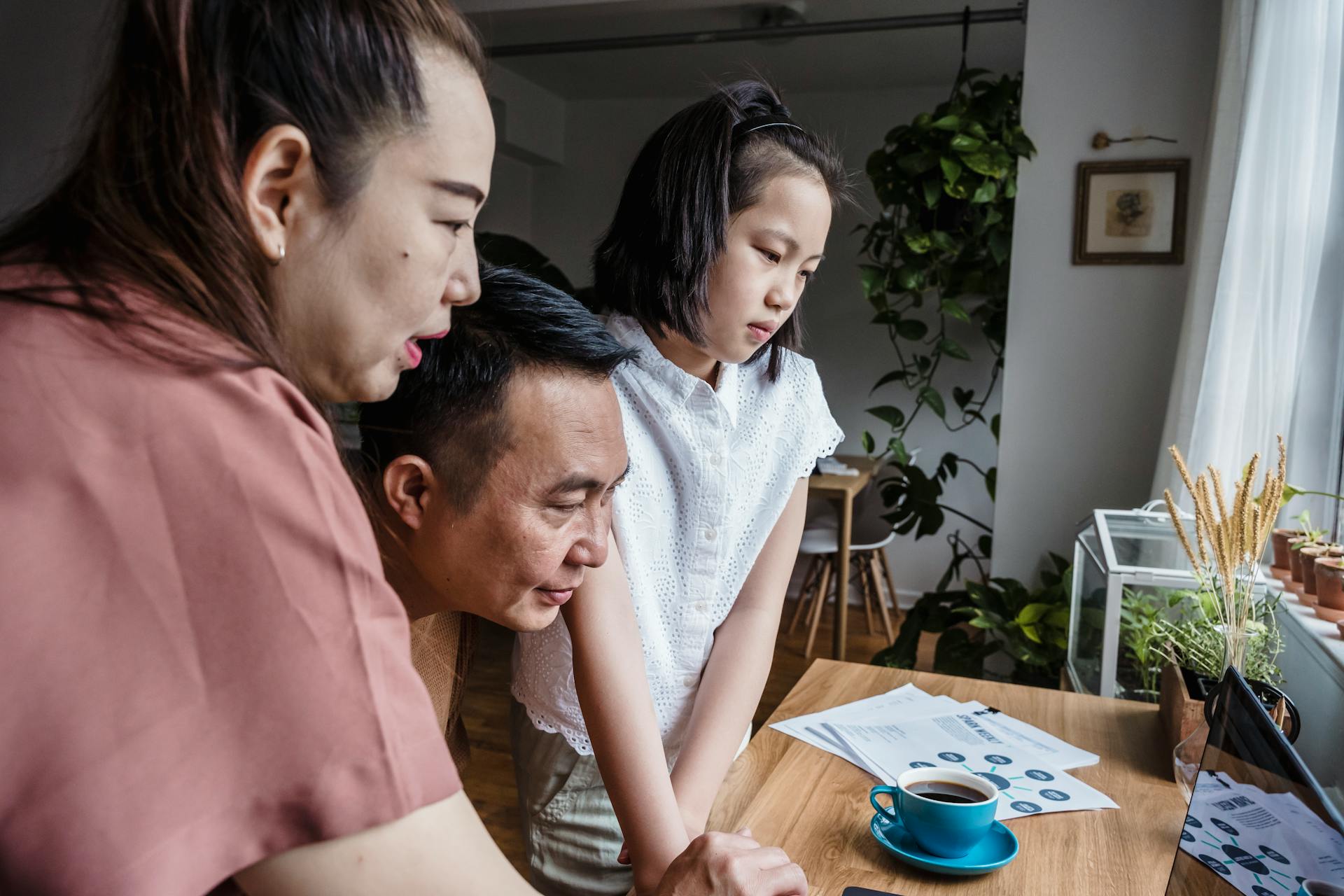 Asian family working together on a home project using a computer and notes.