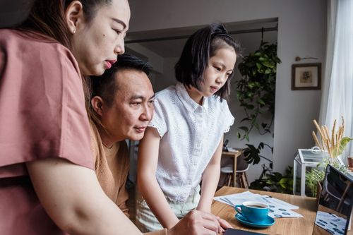 Free A family of three engaged with a laptop in a cozy home setting filled with houseplants. Stock Photo
