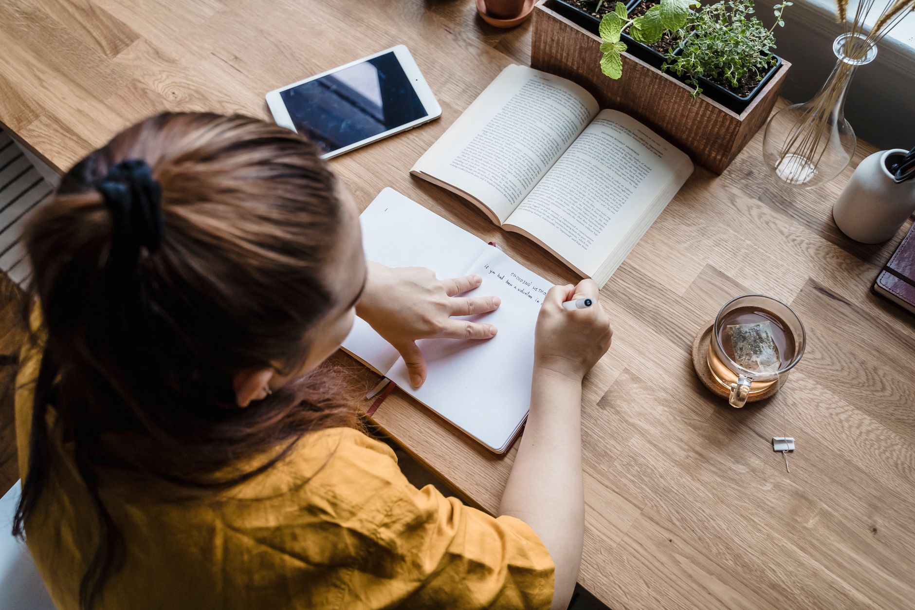 Notebook, tea and a tablet on a wooden desk, the kind of low-stimulation setup that makes staying in feel deliberate rather than dull.