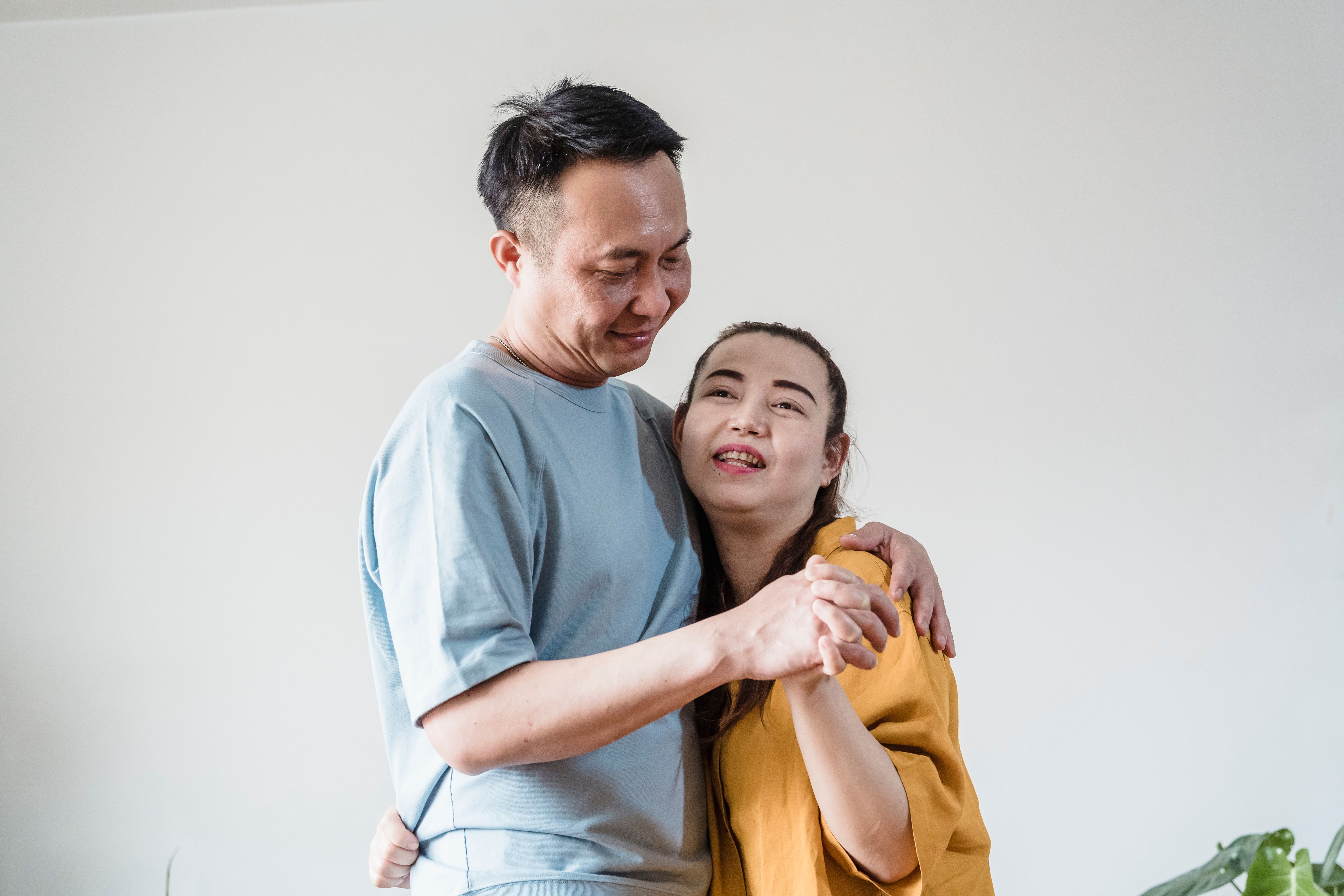 Happy Asian couple holding hands and sharing a warm embrace indoors.