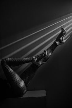 Black and white image of legs in fishnet stockings and high heels, showcasing elegance and fashion.