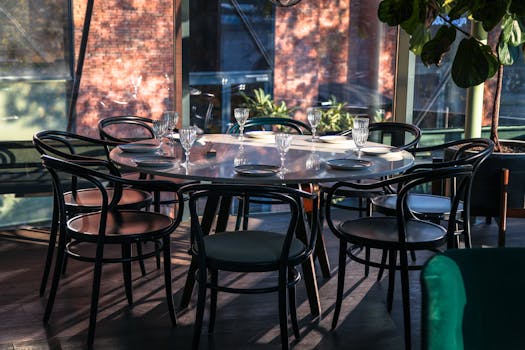 Stylish outdoor café setting with elegant chairs and table set for diners, bathed in sunlight.