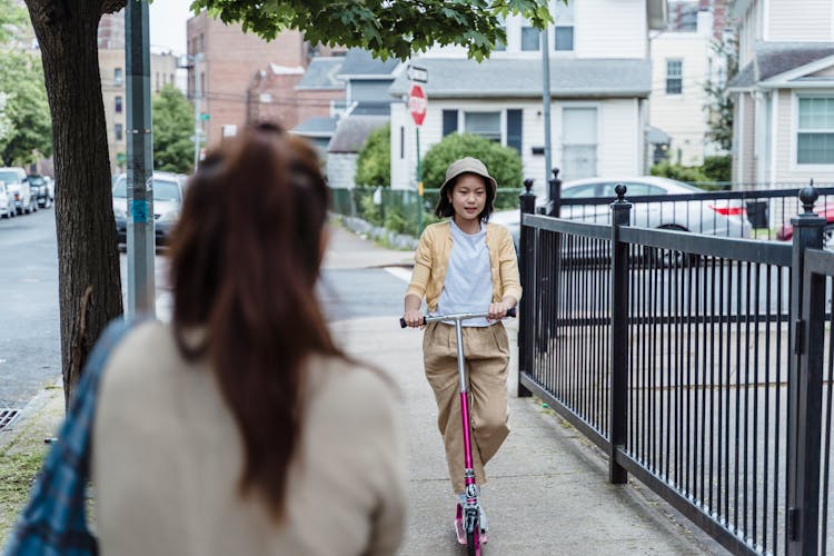 Girl Riding On A Scooter On A Sidewalk In City 