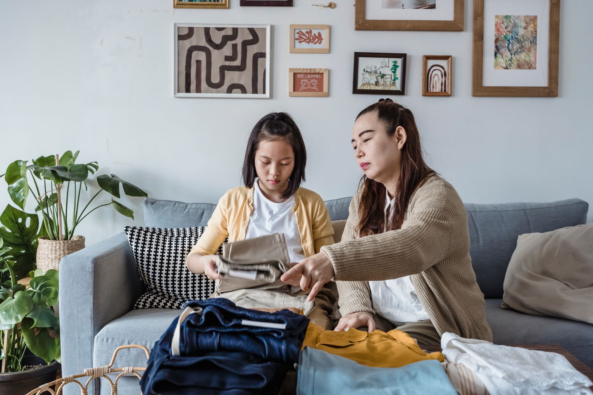 Mother and daughter folding laundry on a sofa in a cozy home interior setting, showcasing family bonding.