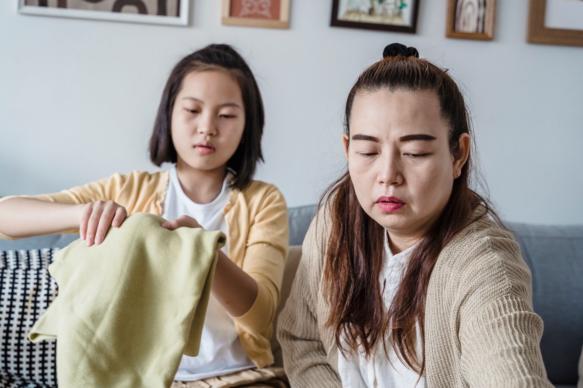 Asian mother and daughter folding clothes together, enjoying quality time at home.