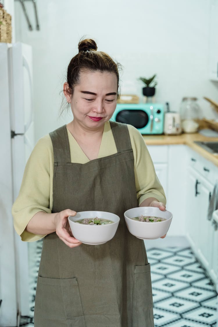 Woman Wearing Apron Carrying Bowls Of Soup