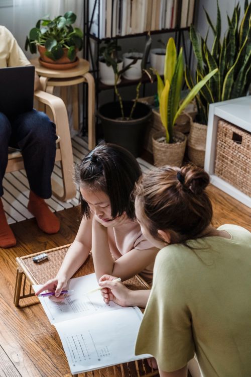 Free A mother assists her daughter with schoolwork in a cozy living room setting. Stock Photo