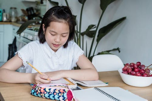 Free A Girl in White Top Writing on a Notebook Stock Photo