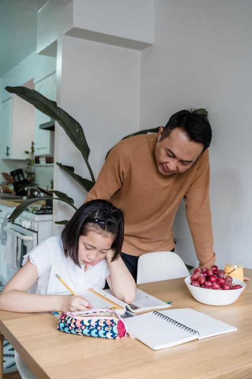 Free Father helping daughter with homework in kitchen setting, fostering education and family bonding. Stock Photo