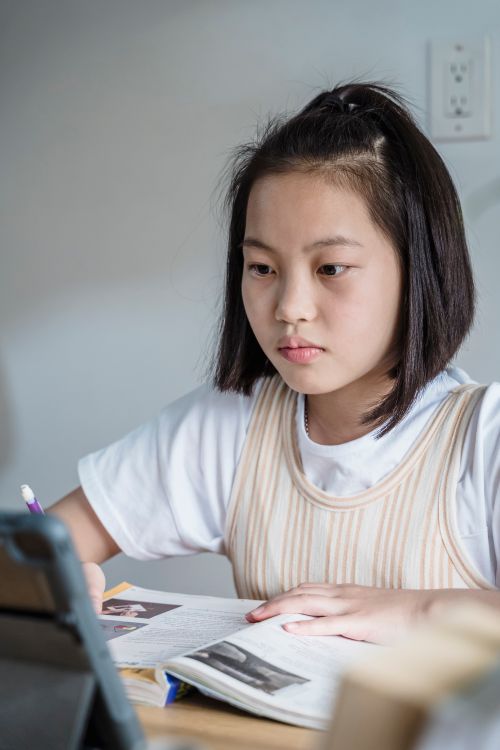 Free A teenager deeply focused on studying with a tablet and open books indoors. Stock Photo