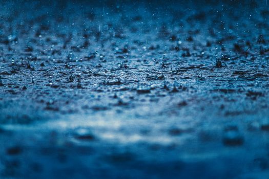 Close-up view of raindrops creating ripples on a surface during a rainy day.