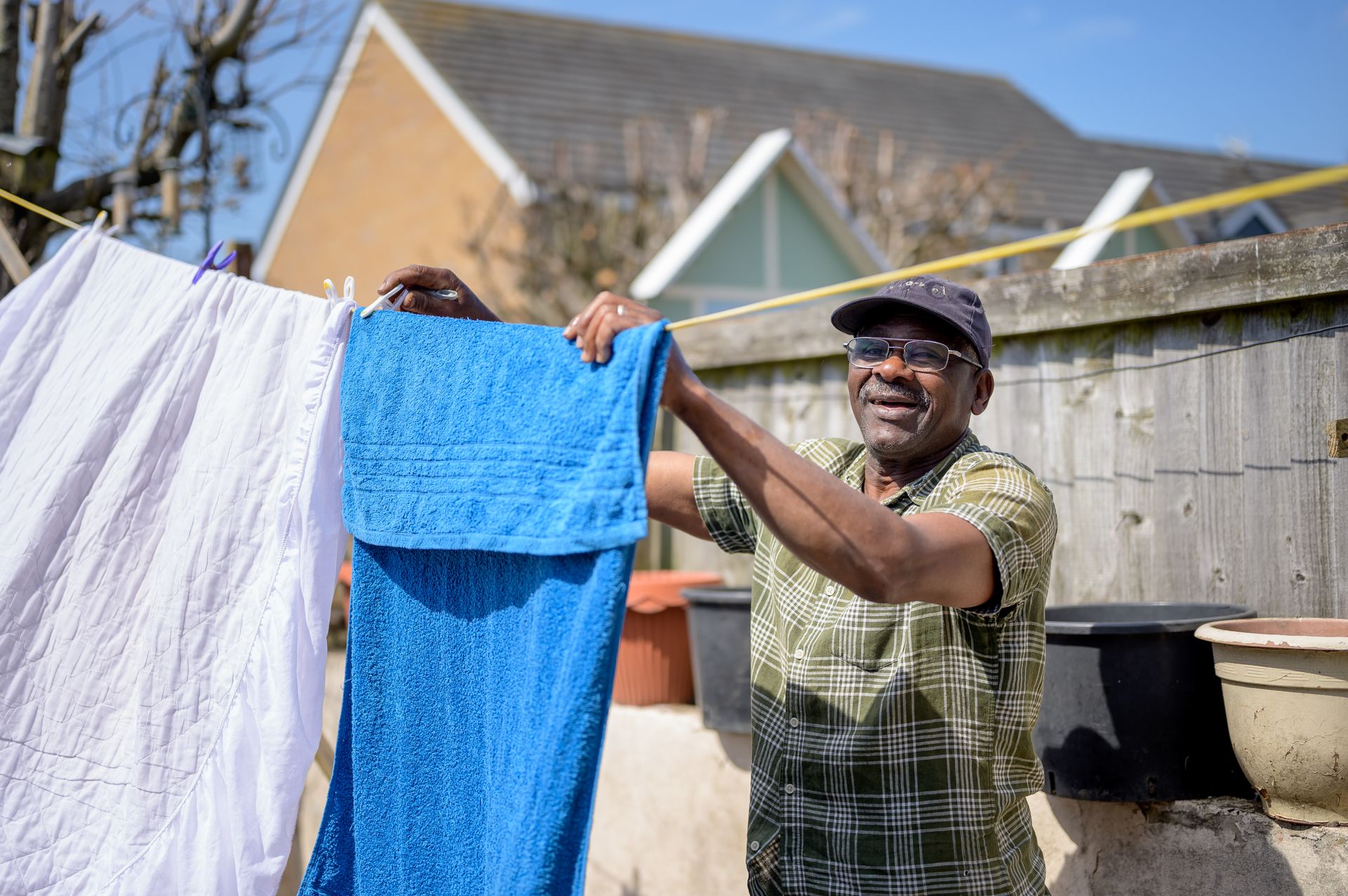 Senior man smiling while hanging laundry outside on a bright sunny day, showcasing a cheerful lifestyle.