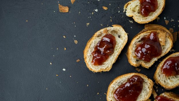 Top view of sliced bread with strawberry jam and crumbs on a dark background.
