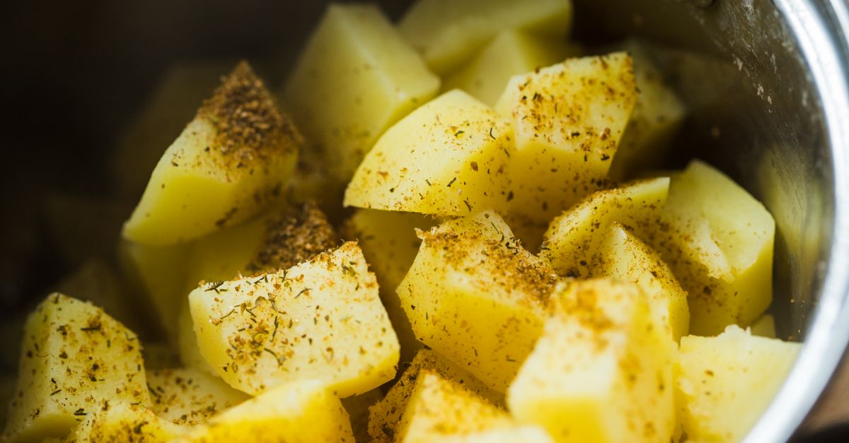 Close-up de pedaços de batata temperados em uma panela de metal, prontos para servir.