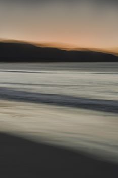 A serene beach scene at sunset with blurred waves and distant mountains in Florianópolis.