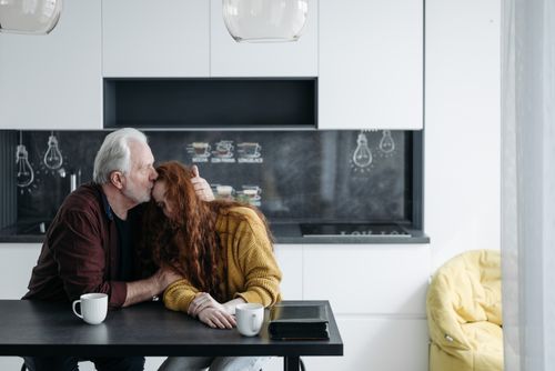 Free An elderly man lovingly kisses his granddaughter on the forehead in a modern kitchen setting. Stock Photo