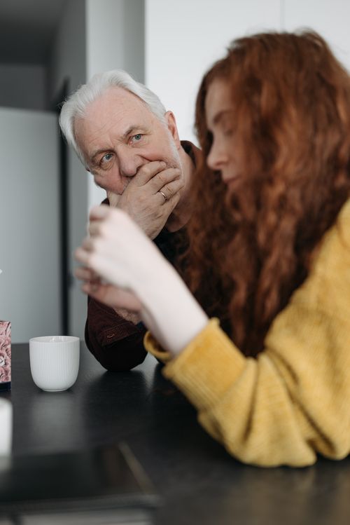 Free An elderly man and a young woman share a thoughtful conversation at a kitchen countertop. Stock Photo
