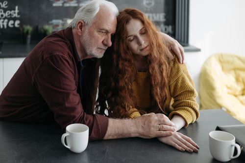 Free An elderly man consoles a young woman at a table in a warm, intimate indoor setting. Stock Photo
