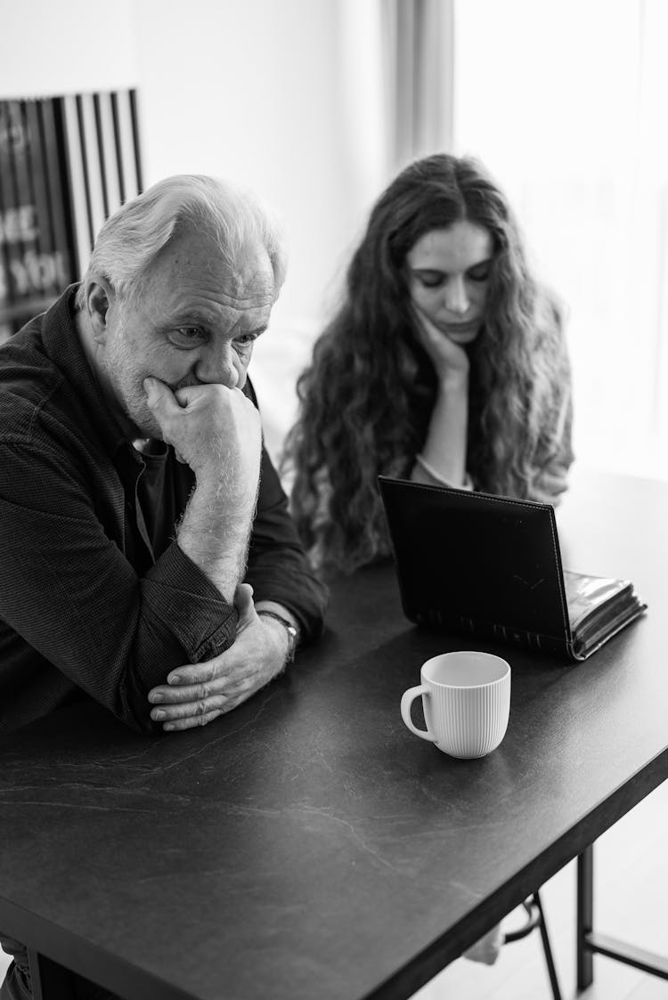 Angry Mature Man And Woman Sitting On Table With Photoalbum