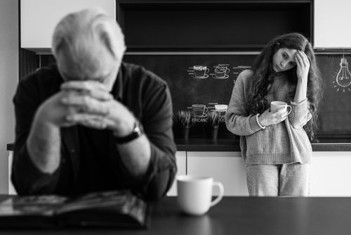 Free A man and woman in a kitchen reflect with mugs, conveying emotions. Stock Photo